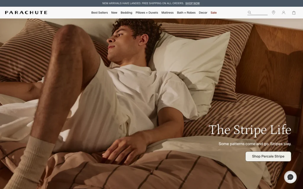 Parachute Home homepage screenshot — 'The Stripe Life' lifestyle imagery in a sunlit bedroom with model on striped bedding.
